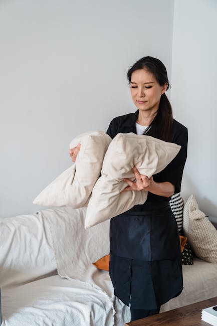 A white fabric sofa covered with a protective sheet or slipcover, situated in a room with neutral-colored walls. To the right of the sofa, there are three stacked cardboard boxes of varying sizes, lik